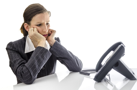 Sad businesswoman sitting at white office desk waiting for a phone call.